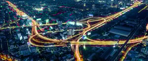 Ein gelb beleuchtetes Autobahnnetzt liegt inmitten von der Dämmerung blau gefärbter Gebäude und Hochhäuser. Das Bild repräsentiert die neu entstandenen Verbindungen zwischen bluepool und ET GLOBAL.