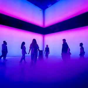 An artificial space created by LED walls glowing in blue and violet. The room is foggy, and silhouettes of people are visible.
