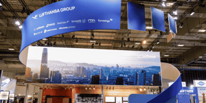 Main view of the Lufthansa Group stand at the ITB tourism trade fair, featuring a large ring-shaped structure on the ceiling and a large LED display.