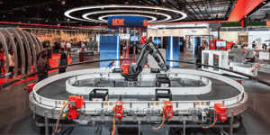An automated conveyor system featuring industrial robots and drive technology, showcased as an interactive product demonstration at the SEW-EURODRIVE stand during the Hannover Messe trade fair for mechanical engineering and automation.
