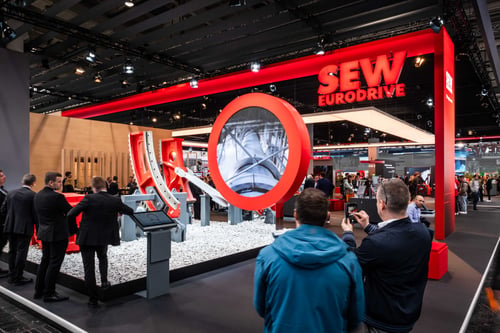 Ansicht des SEW-EURODRIVE Messestandes 2024 auf der Hannover Messe mit einem runden LED-Display sowie einem großen Logo und roten Konstruktionselementen.