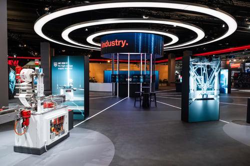SEW-EURODRIVE-Messestand mit Cockpit-Bauelement zentral auf der Standfläche sowie LED-Display-Aufstellern und zyklischen Design- und Lichtelementen.