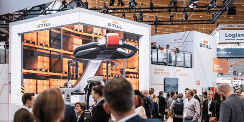 Ansicht des STILL Messestandes 2024 auf der LogiMAT mit einer großen übers Eck gehenden LED-Wand, die zahlreiche Besucher anzieht.