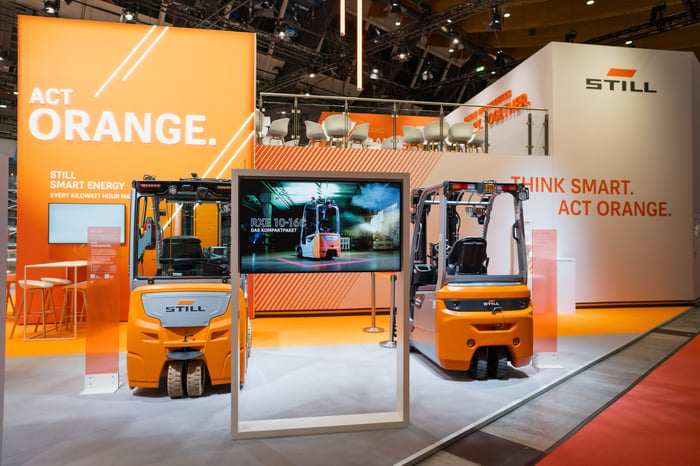 Ansicht des STILL Messestandes 2026 auf der LogiMAT mit Gabelstaplern als Exponate, einem doppelstöckigen Messebau mit Balkon und orange-weißen-Designelementen.