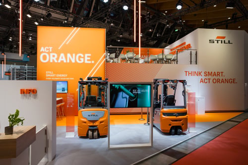 Modernes Messestand-Design für STILL mit bedruckten Grafik-Wänden, Flächen für Besprechungen, Exponaten und Glasgeländern.