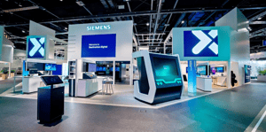 Siemens-Messestand mit großem Logo und digitalen Präsentationsflächen. Mehrere Monitore zeigen Inhalte zu nachhaltiger und digitaler Mobilität. Der Stand ist offen gestaltet mit klaren Linien und moderner Architektur.