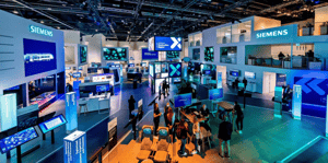 Großer Siemens-Messestand auf der InnoTrans mit modernen Displays, interaktiven Touchscreens und Sitzbereich. Mehrere Besucher bewegen sich durch den offenen, hell beleuchteten Stand mit blauen und weißen Markenfarben.