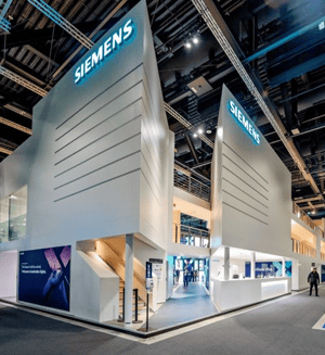 Siemens-Stand auf der InnoTrans mit hohen weißen Wänden und prominentem Logo. Der Bereich ist hell ausgeleuchtet und zeigt eine Kombination aus Architektur und Technologie-Displays.
