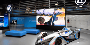 Ausschnitt des ZF Messestandes auf der Automechanika mit Formel 1 Auto und blauen Sitzmöglichkeiten.