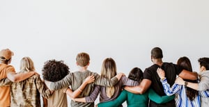 Blick von hinten auf Menschen unterschiedlicher Ethnien und Kulturen, die sich gegenseitig an die Schultern fassen.