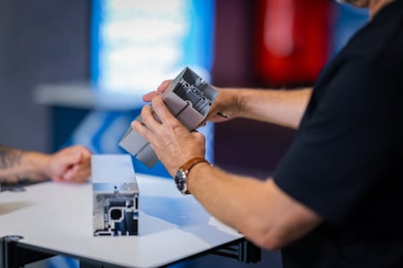 Hände montieren und demonstrieren ein octanorm Aluminiumprofil auf einem Tisch, das als technisches Systemelement für modulare Markenräume im Messebau eingesetzt wird.