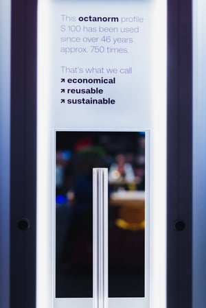 Beleuchtete Stele mit octanorm Systemprofil und Text zur Wiederverwendbarkeit seit über 46 Jahren, visualisiert nachhaltige modulare Markenräume im Messebau.