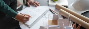 A view of a workspace featuring various sketches, an architectural model and other working materials.
