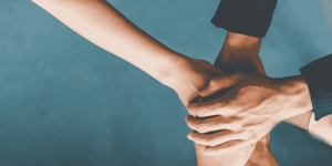 Arms extend into the picture from several directions. The hands are resting on top of one another.