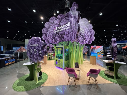 Messestand von Broccoli AI mit einem großen stilisierten Brokkoli-Bau mittig auf der Standfläche.