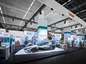 Bosch Messestand auf der Automechanika-Messe mit Formel-1-Auto im Vordergrund und weißen Designelementen.