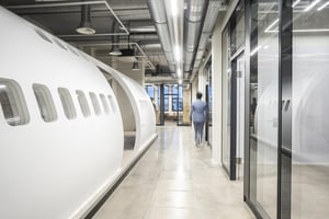 Modern office featuring airplane fuselage design with window sections, bright hallway with industrial lighting and exposed ducts, person walking down the corridor.