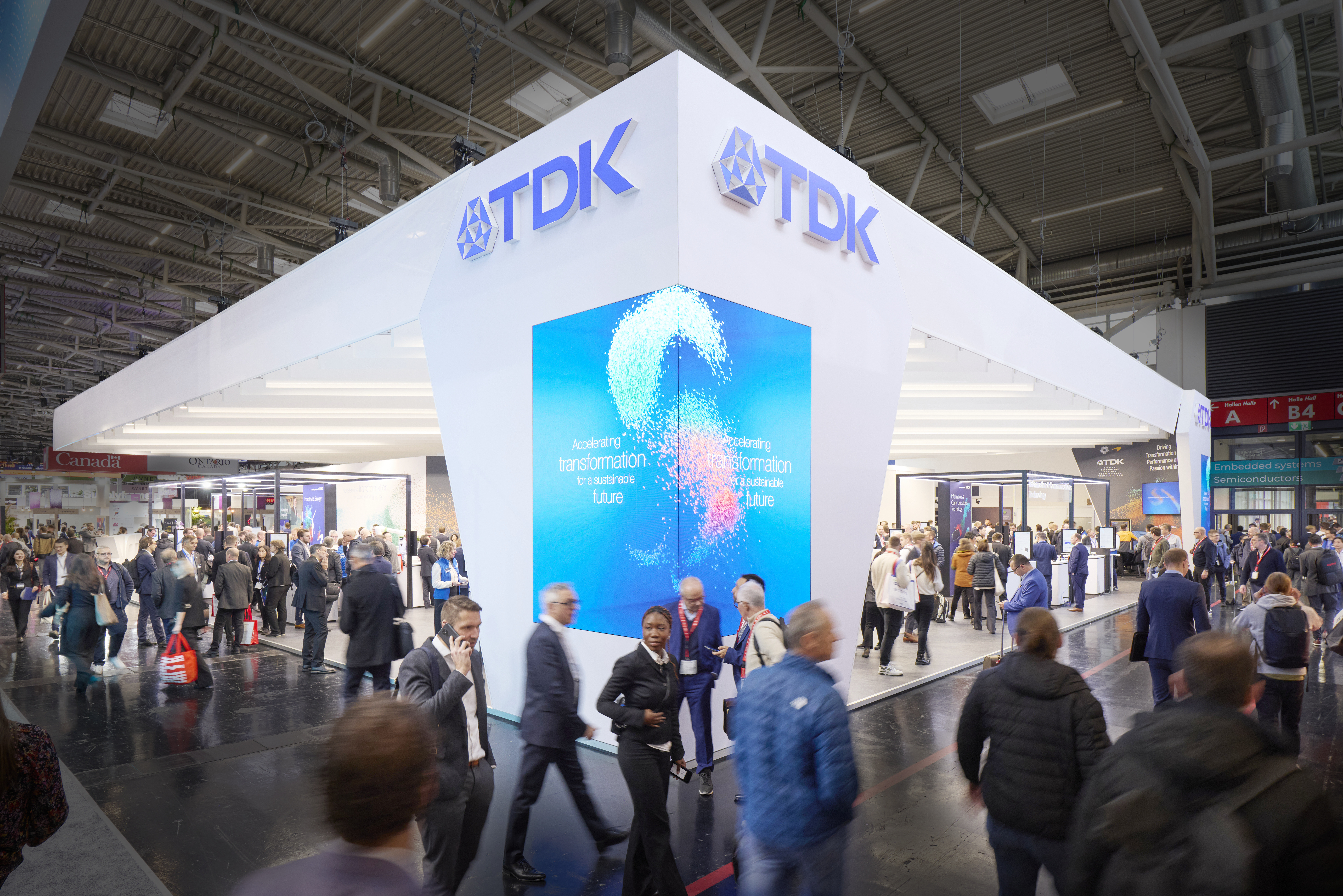 TDK exhibition stand at electronica 2025 with white walls and a big LED display that goes around the corner.